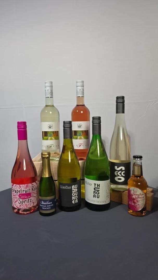 Vielfalt an Weinen und Schaumweinen in verschiedenen Flaschen auf grauem Hintergrund.